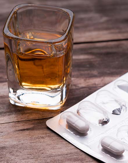 стакан с алкоголем и таблетки в упаковке на столе